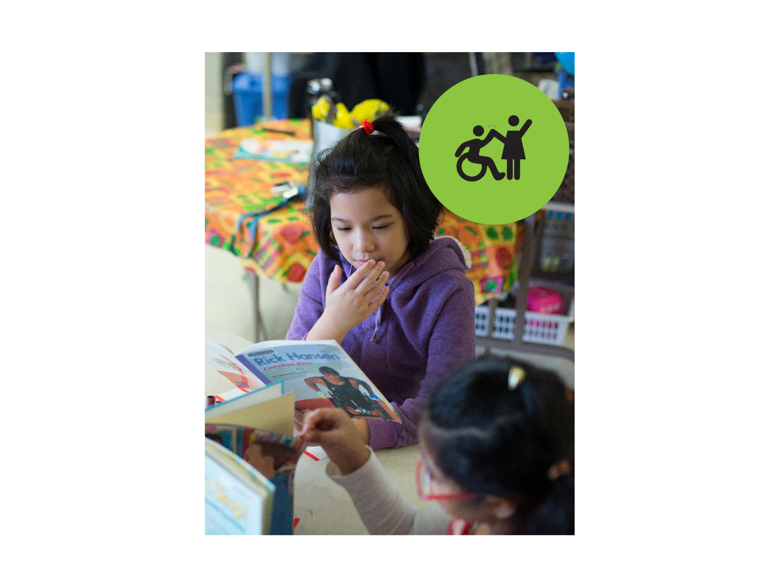 Young teen sitting at a table and reading a copy of the book "Rick Hansen Canadian Hero". Small green circle icon with graphic of person in a wheelchair high-fiving a person that is standing.