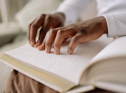 A braille book open on a person's lap, being read with their fingers, in a room full of natural light 