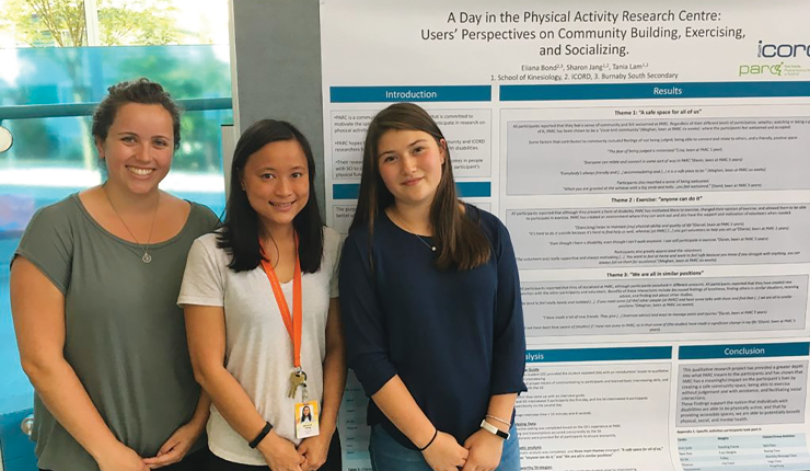 three woman, smiling, in front of research poster