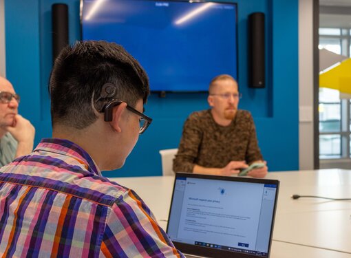 three men at a board room table, using hearing aids