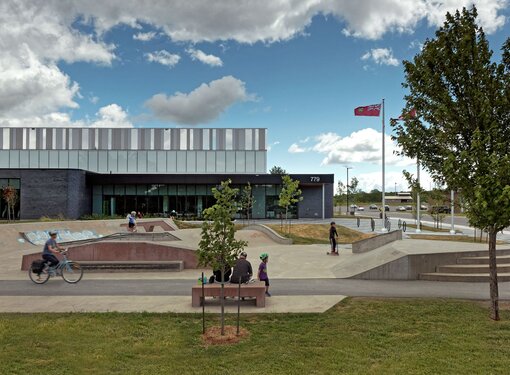 An outside view of Kingston East Community Centre. There are people outside using the accessible pathways and ramps, and benches. 