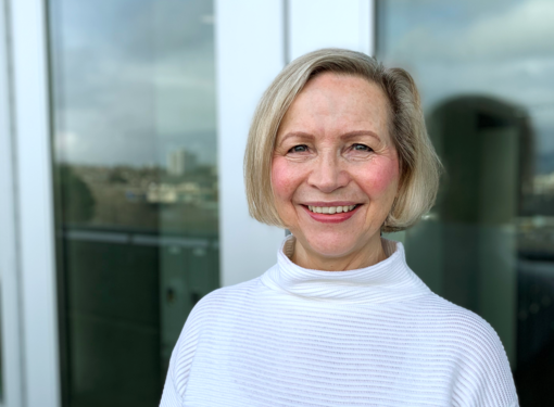 Pat Short wearing a white turtleneck sweater and smiling at the camera. Pat has chin-length light coloured hair.